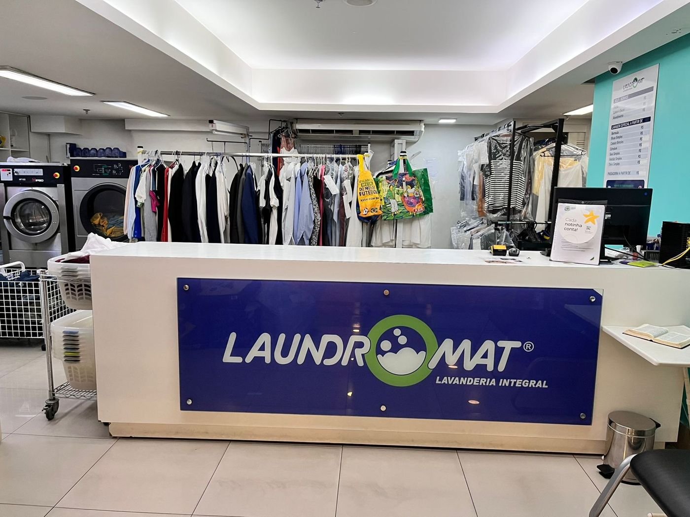 Balcão de atendimento da lavanderia Laundromat no Setor Bueno, dentro do Goiânia Shopping, com roupas sociais passadas e embaladas ao fundo